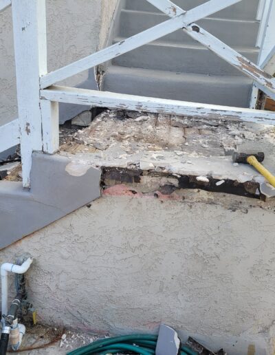 Damaged outdoor stairway with crumbling concrete and exposed rebar, alongside tools for repair.