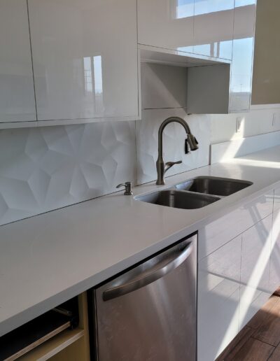 Modern kitchen with white cabinetry, stainless steel sink, and sunlight casting shadows on the countertop.