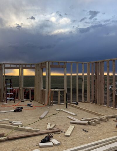 Construction of a wooden framed building under a dramatic cloudy sky at sunset.