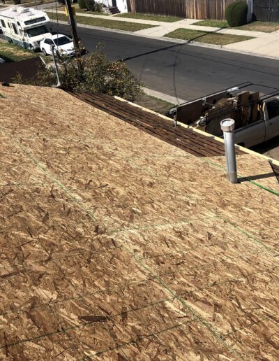 New plywood sheathing on a residential roof with a truck parked below on a sunny day.