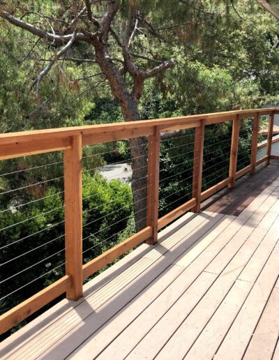 Wooden deck with a cable railing overlooking greenery.