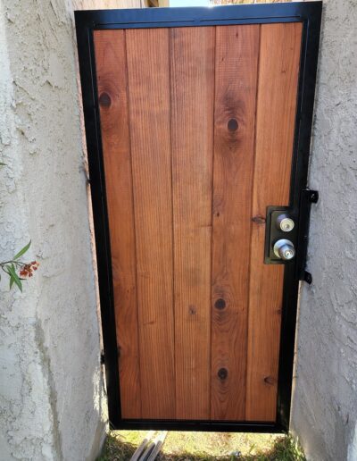 A wooden door with a metal frame and a silver doorknob set in an outdoor wall.