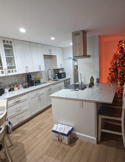 Modern kitchen with white cabinets and a christmas tree decorated with red ornaments.