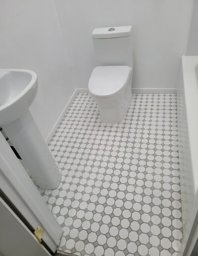 A compact bathroom with a white toilet and pedestal sink, featuring hexagonal floor tiles.