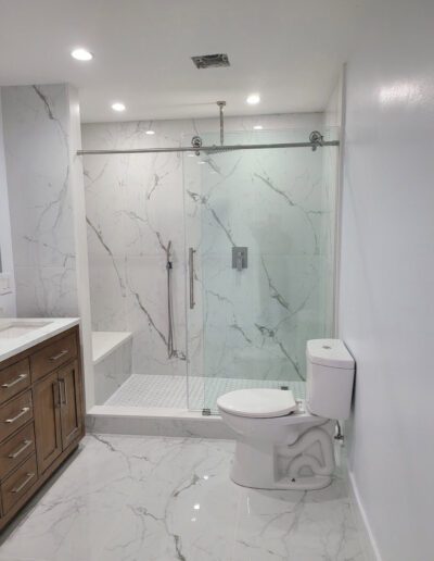 Modern bathroom with marble tiles featuring a glass-enclosed shower and a wooden vanity.