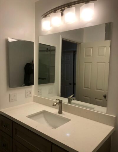 Bathroom interior showing a vanity with a sink, faucet, and mirror with overhead lighting.