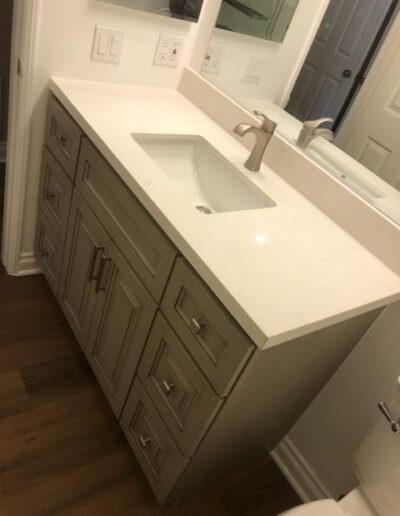 A modern bathroom vanity with a white countertop and built-in sink, featuring storage drawers and cabinets.