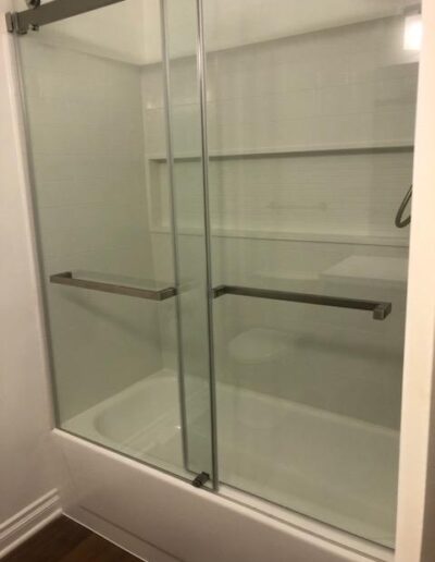 A clean, white-tiled shower with clear glass doors and metallic handles.