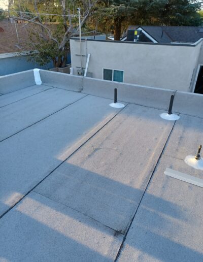 Flat rooftop with vent pipes and surrounding residential buildings during dusk.