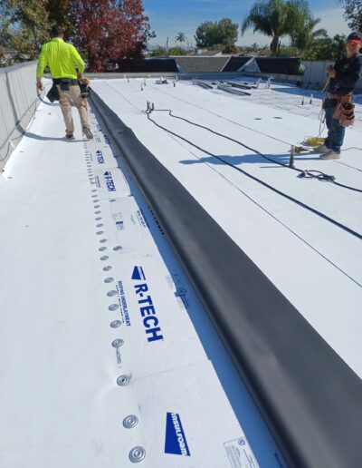 Workers installing waterproofing membrane on a flat roof.