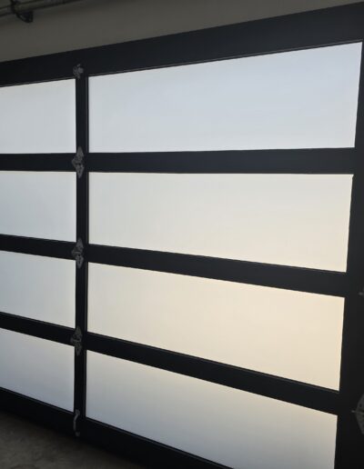 Frosted glass garage door with five horizontal panels and black metal frame, viewed from the inside.