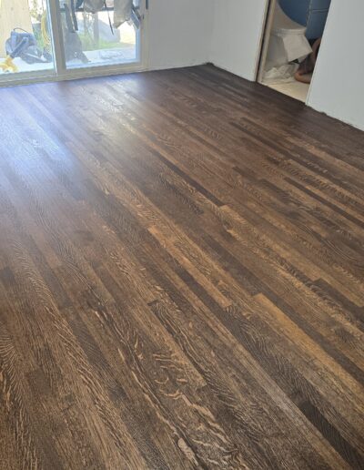 A room with newly installed dark hardwood flooring and an unfinished wall. A sliding glass door is visible in the background.