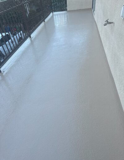 A smooth, freshly coated balcony floor with a metal railing and a faucet attached to the wall.