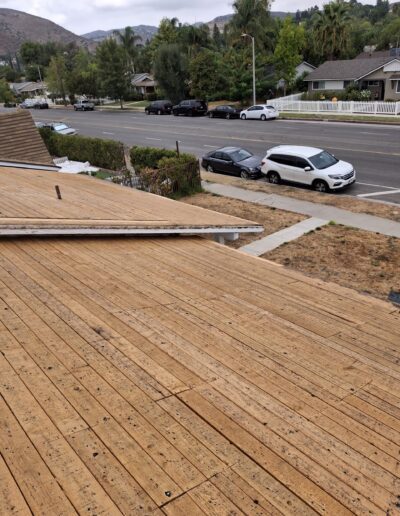 View from wooden roof under construction, facing a suburban street with parked cars and trees in the background.