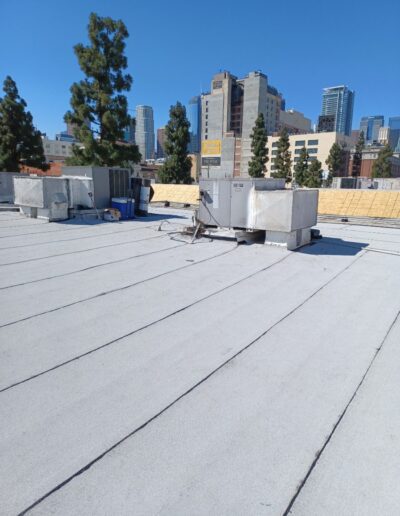 Flat rooftop with HVAC units under a clear blue sky, surrounded by city buildings and trees in the background.